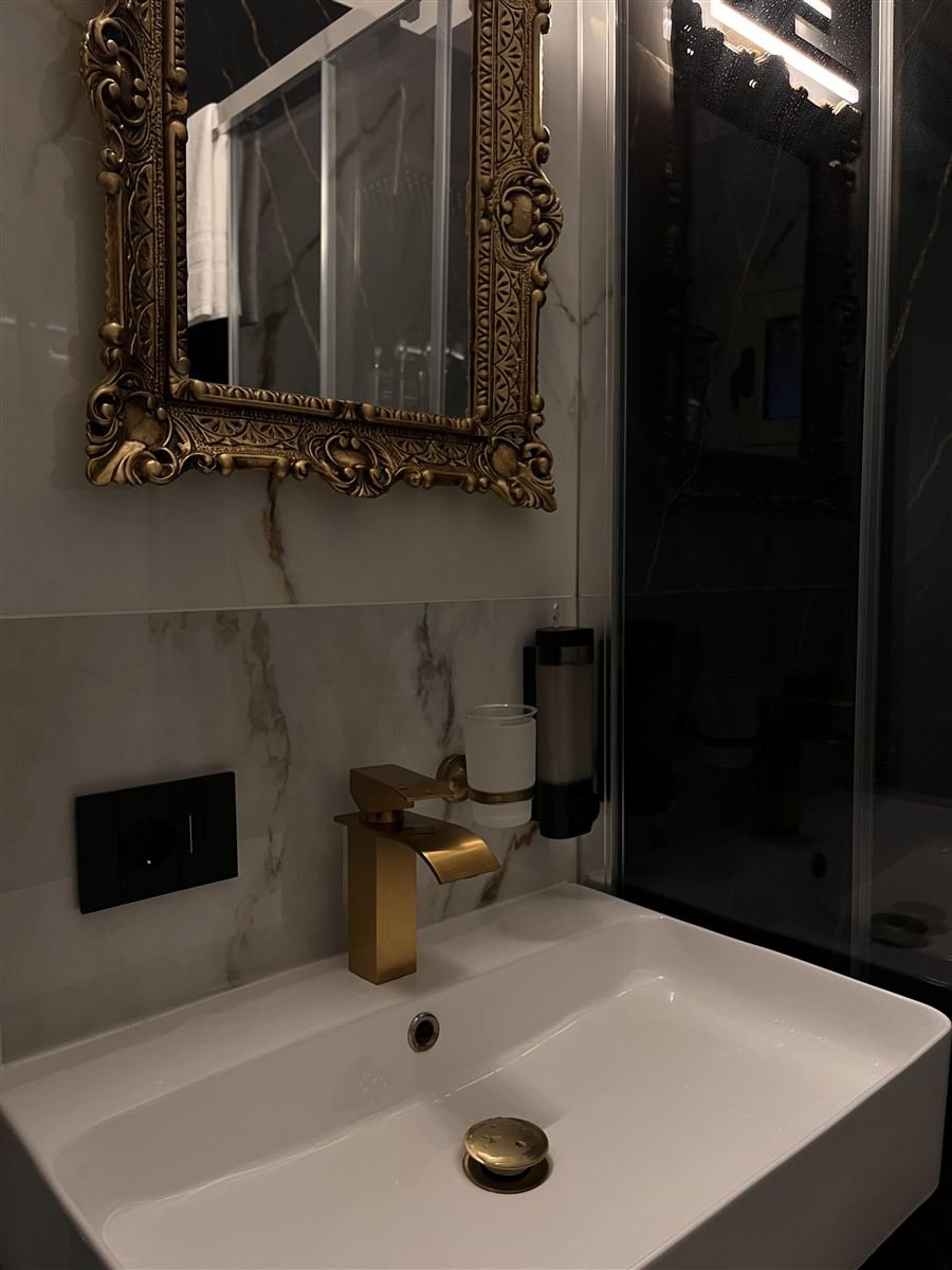 Bagno con specchio dorato intagliato e rubinetteria oro spazzolato